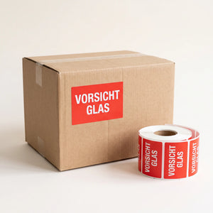 Warnetikett für zerbrechliche Ware: Vorsicht-Glas-Sticker auf einem Versandkarton aufgeklebt, daneben die Etikettenrolle